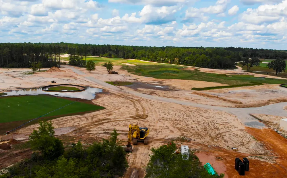 Aerial view of a graded development site with red clay access roads cut between green fields