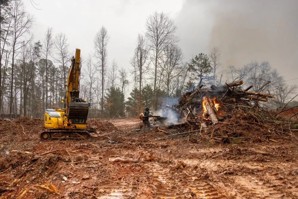 Excavator stacking cut timber onto a burn pile on a freshly cleared lot