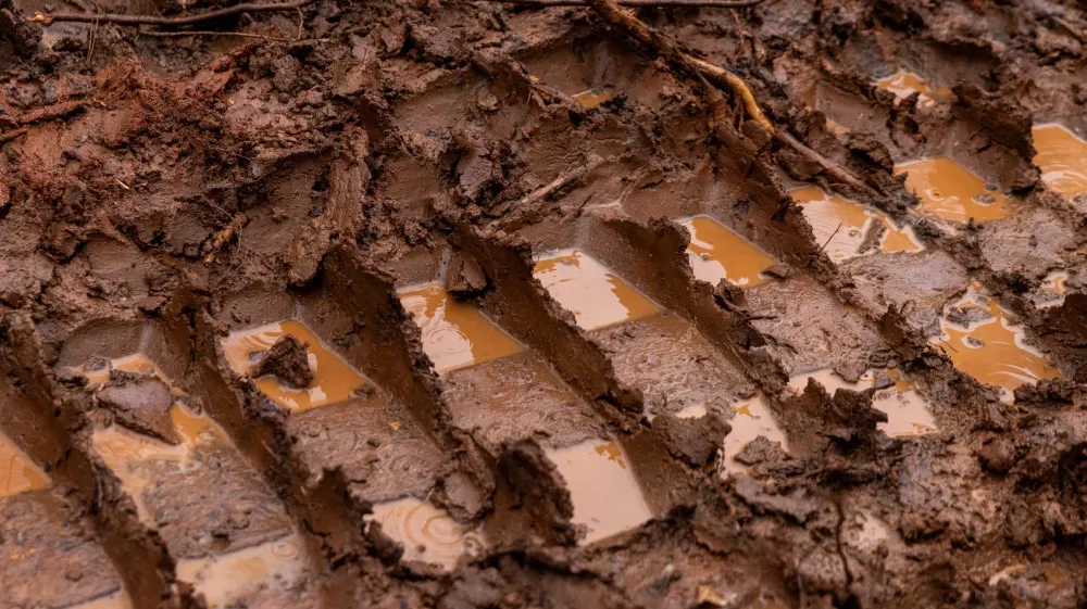 Close-up of deep dozer track ruts pressed into wet red clay