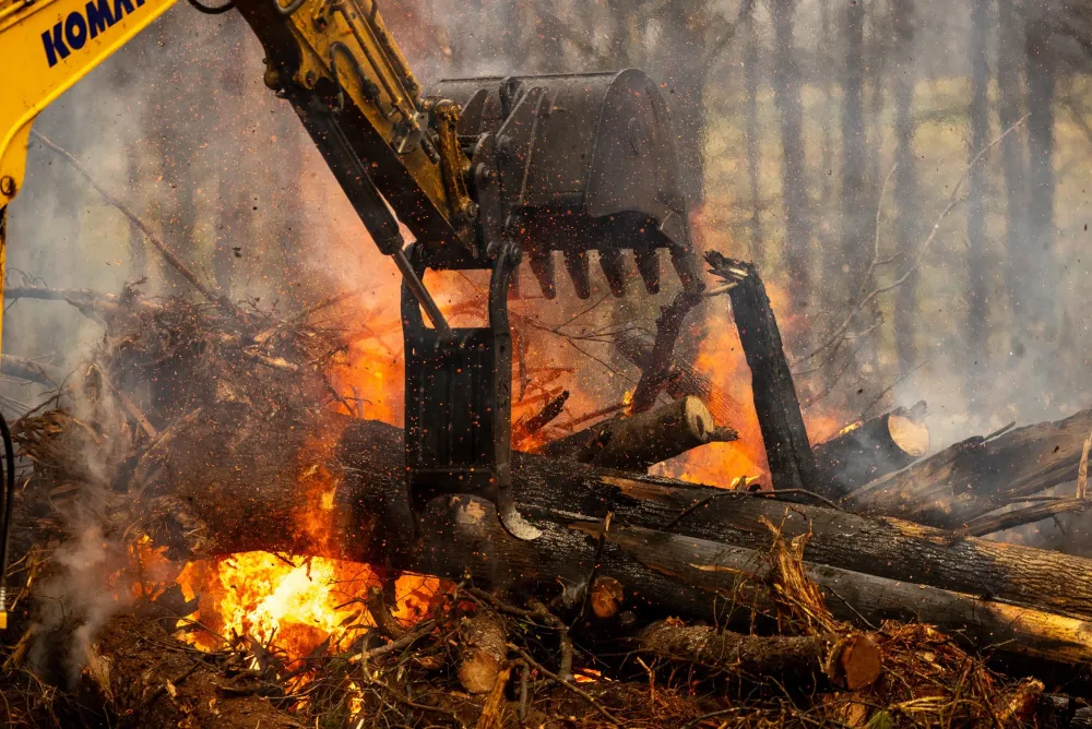 Komatsu excavator feeding logs into an open burn on a land clearing job