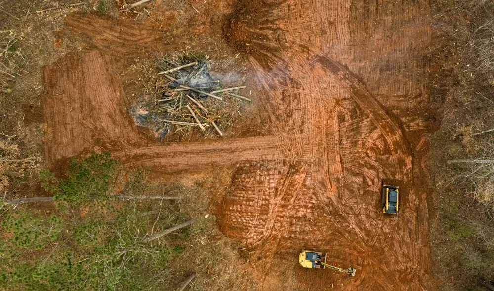 Aerial view of a cleared red clay pad with a stacked brush pile at its center