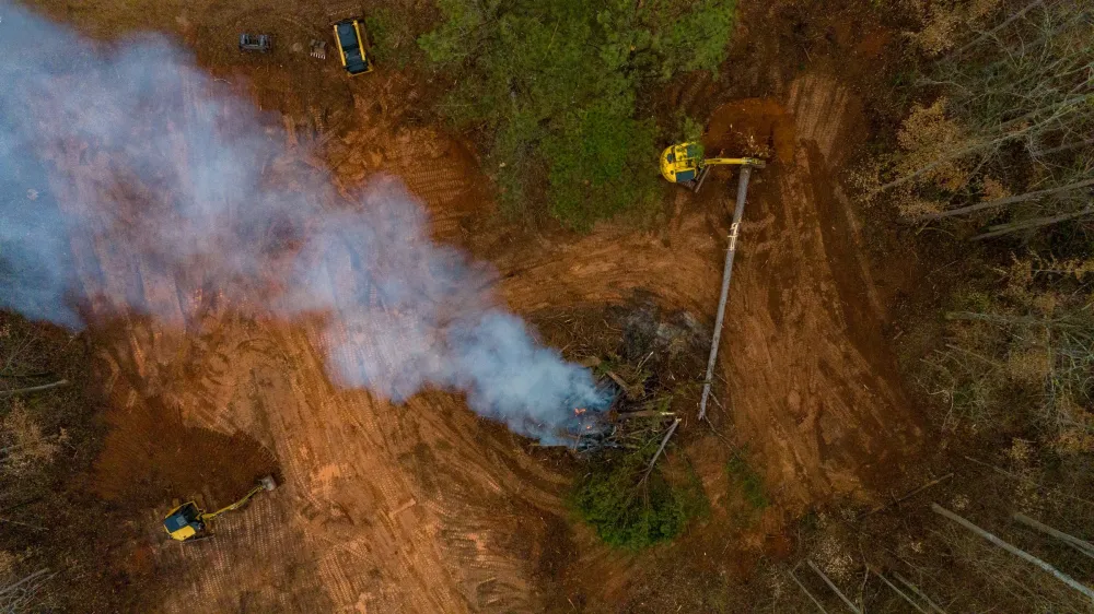 Aerial view of a white smoke column rising from a burn pile in a newly cut clearing