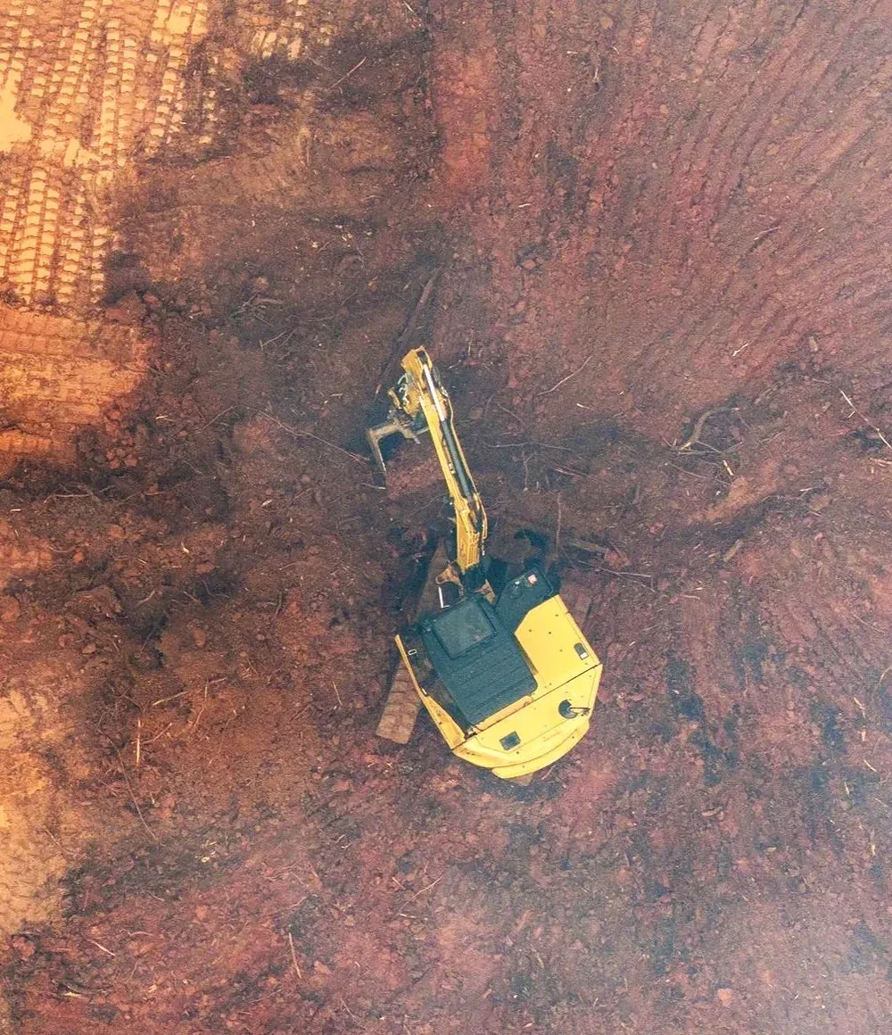 Aerial view of a dozer and excavator shaping a large red clay building pad