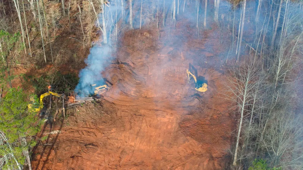 Aerial view of smoke drifting over a red clay clearing being cut out of standing timber
