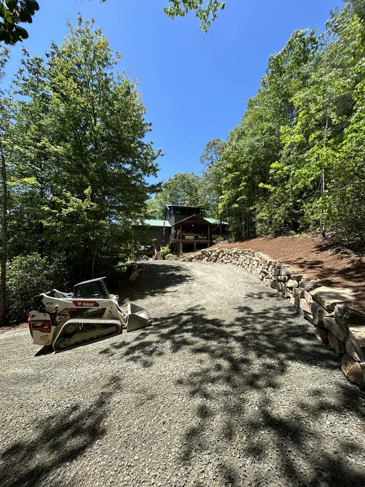 Compact track loader on a newly graded gravel driveway lined with a stone retaining wall